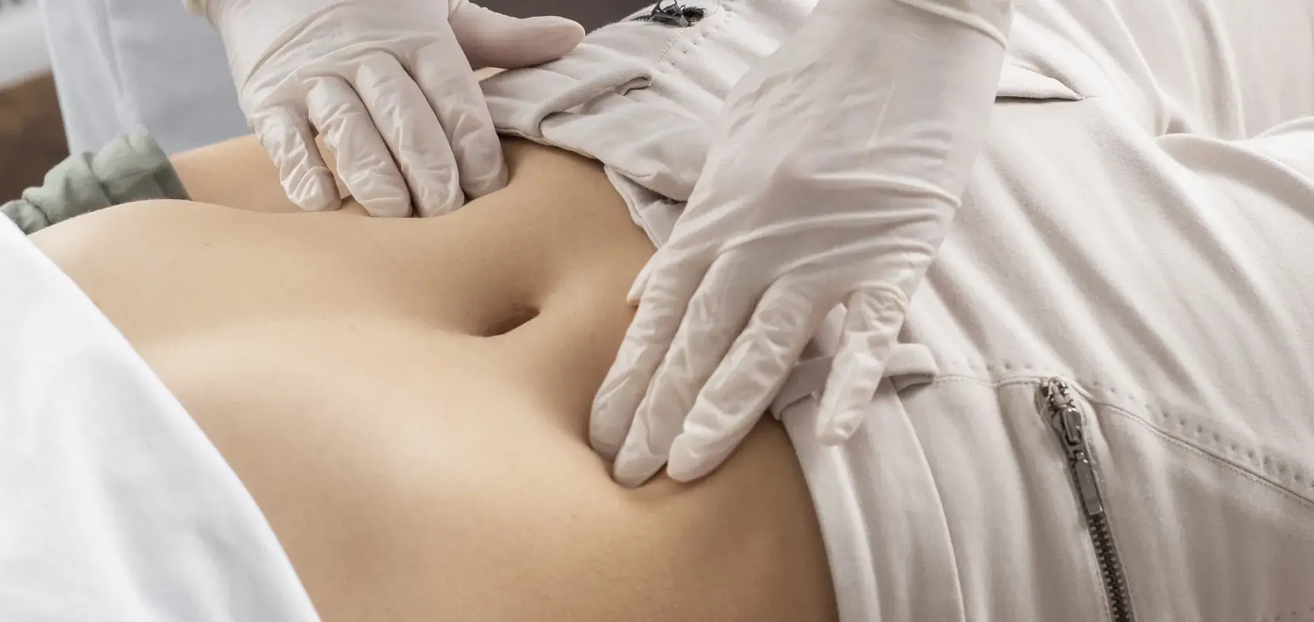 Mani guantate del medico che palpano l'addome di una paziente distesa